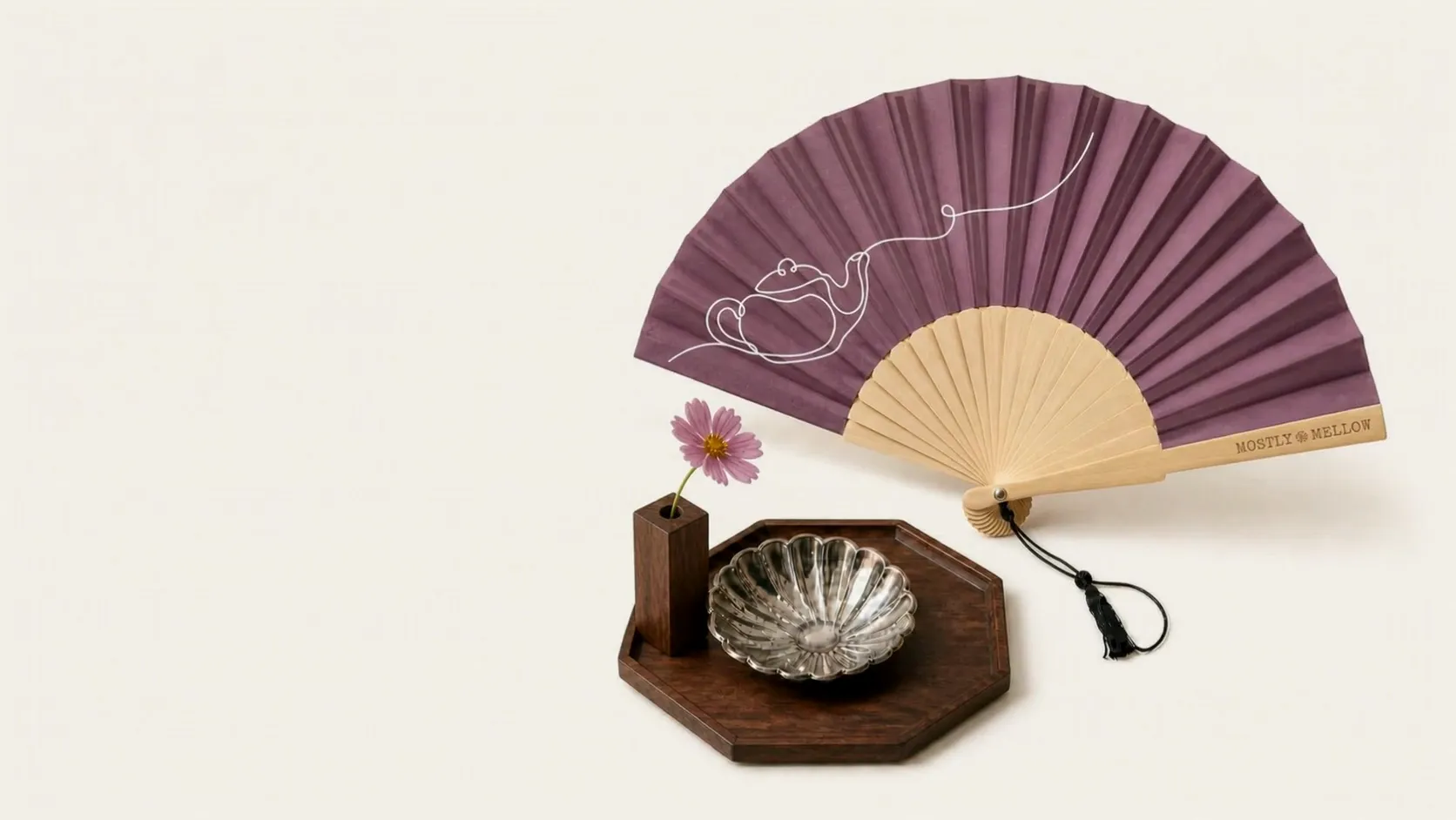 A mauve Mostly Mellow folding fan with white teapot line art above a walnut tray, silver shell dish, and mallow flower in a walnut holder.